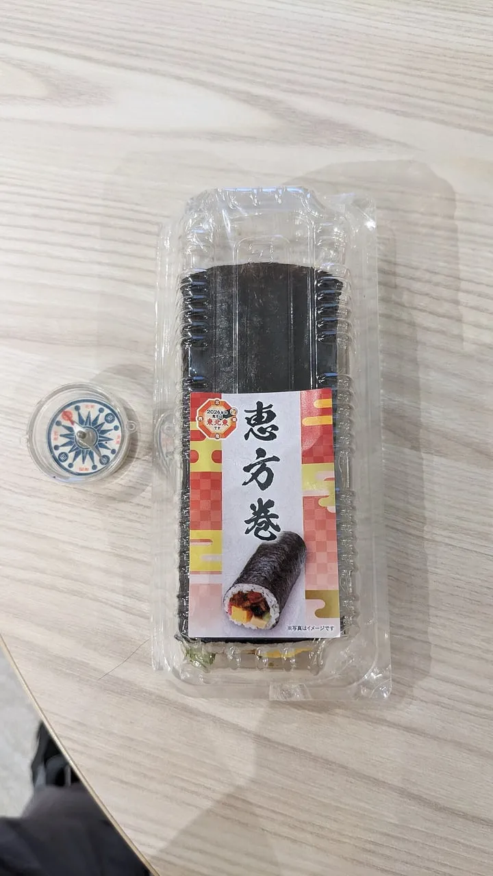 A thick sushi roll in a plastic pack with a label reading ehōmaki, next to a small compass.