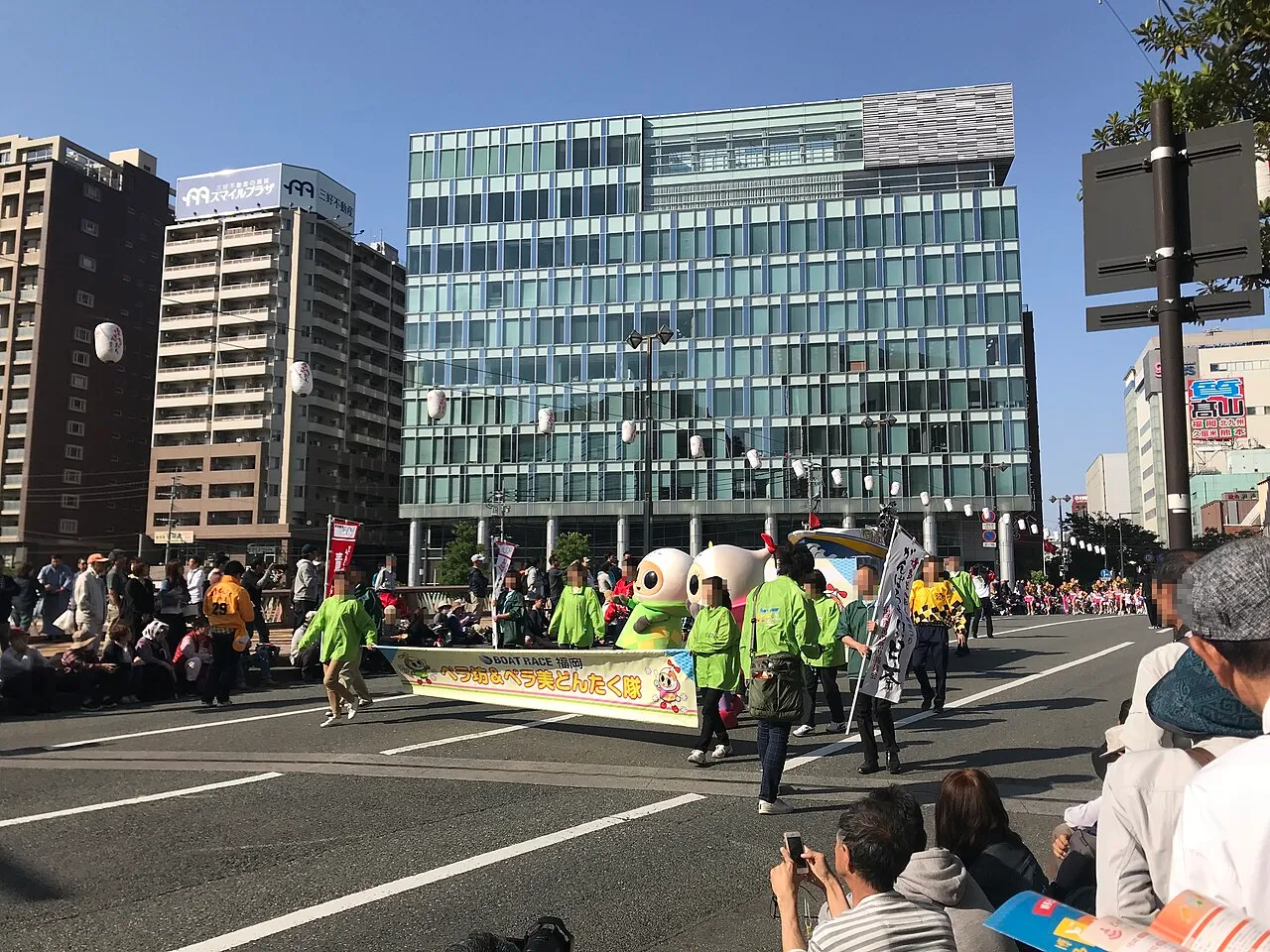 A Dontaku parade group in green costumes walking along a wide city street lined with spectators.