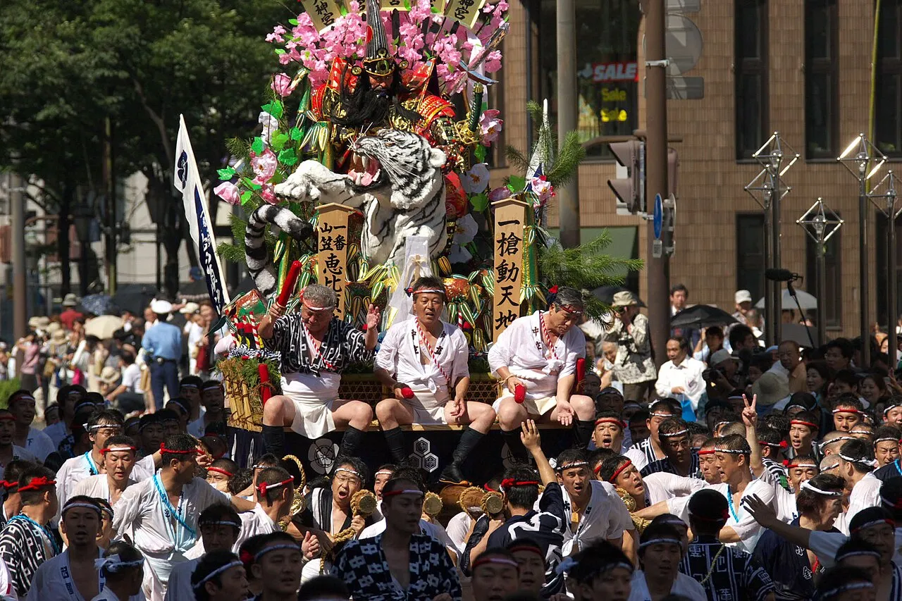 Men in festival dress crowd around a racing yamakasa float topped with warrior figures.