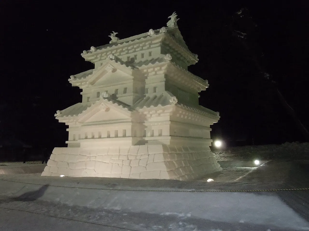 A large sculpture of a castle keep made of snow, lit at night.