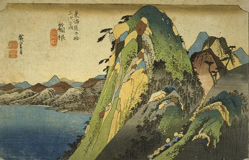 Woodblock print of a towering green and yellow mountain above a blue lake, with a line of travellers climbing the pass at its foot.
