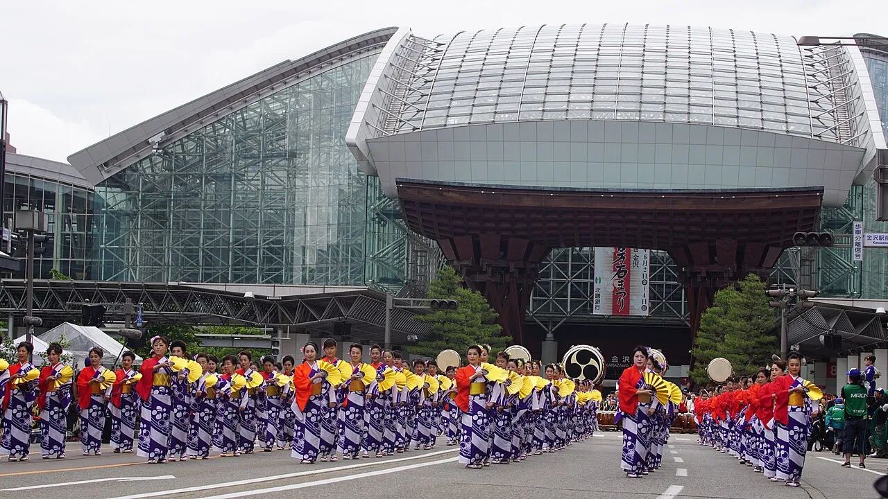 Rows of dancers in matching costumes perform in front of the wooden Tsuzumi Gate of Kanazawa Station.