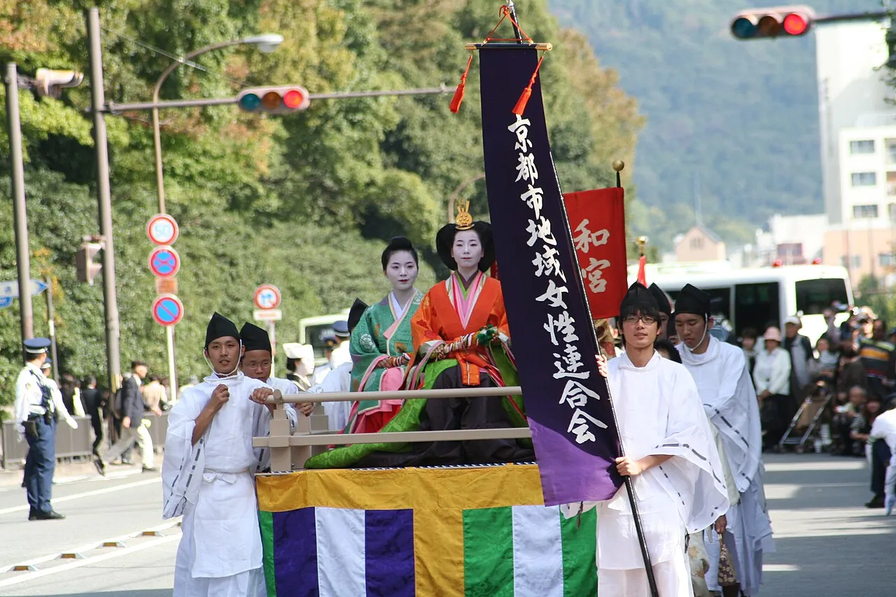 Women in Heian-period court costume ride in a decorated palanquin carried by bearers in white, in the Jidai Matsuri procession.