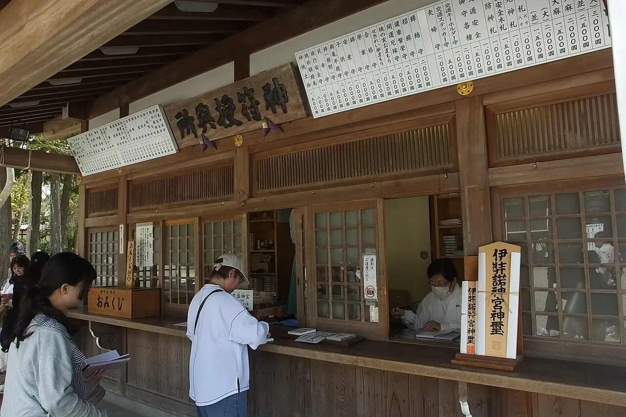 Visitors at the long wooden counter of a shrine office, with price boards above the windows.