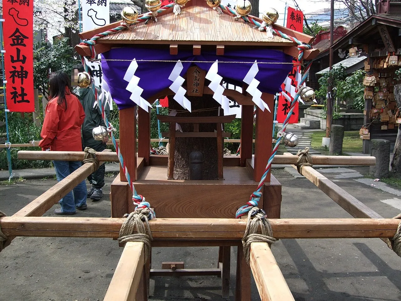 A small wooden mikoshi with a purple curtain and paper streamers on carrying poles.