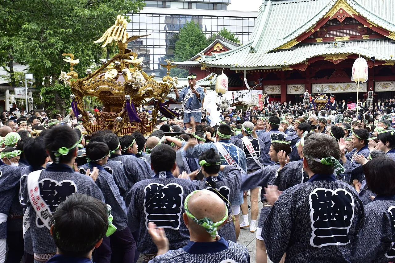 A golden mikoshi carried into the Kanda Myōjin shrine grounds through a dense crowd of carriers in dark happi coats.