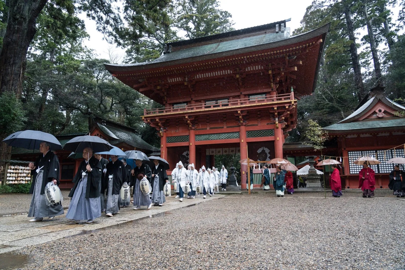 A procession with umbrellas passes the large vermilion gate of Kashima Jingū.