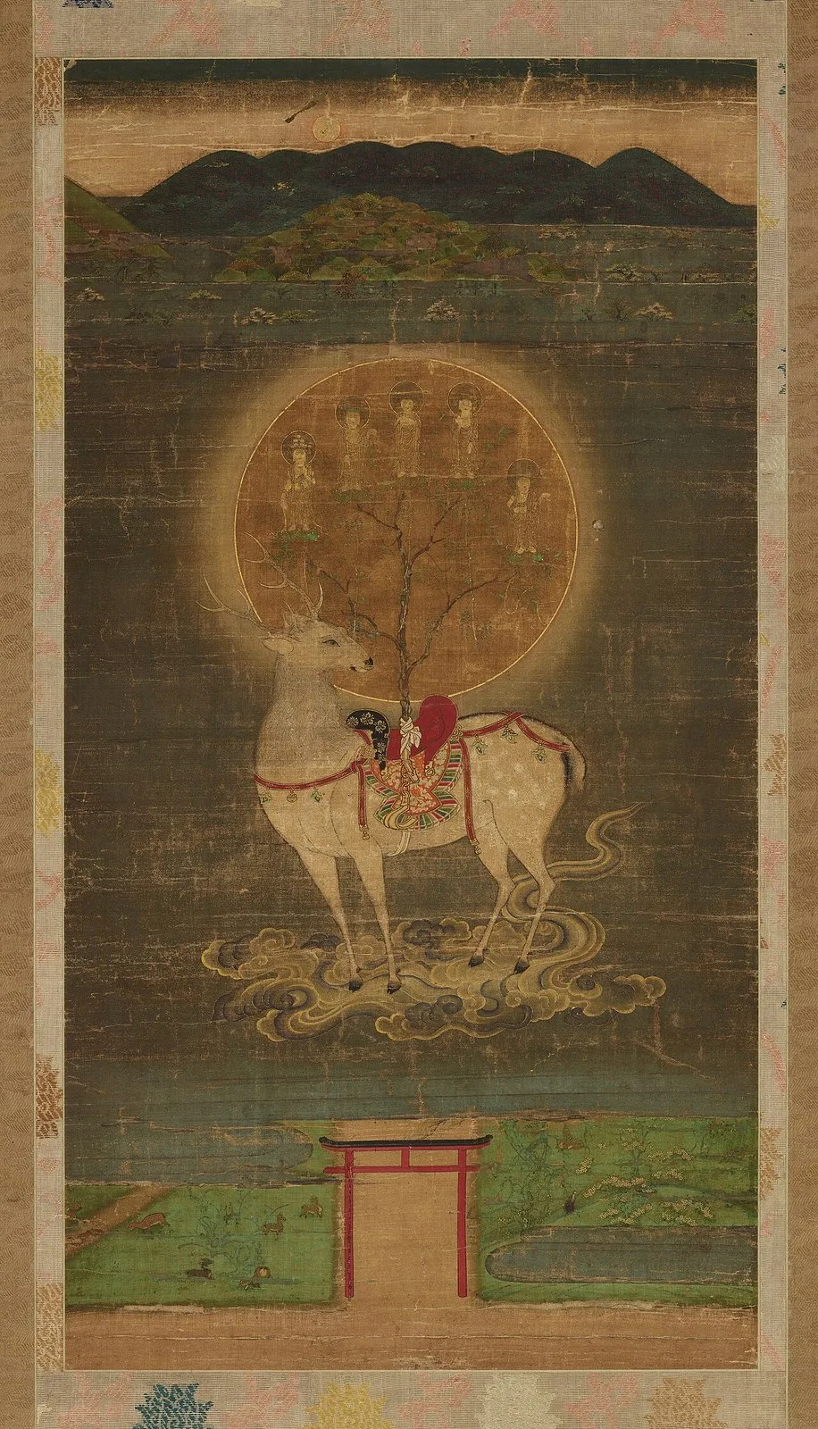 Hanging scroll: a white deer with a saddle carrying a sacred tree and a golden disc stands on clouds above a torii gate, with green hills behind.