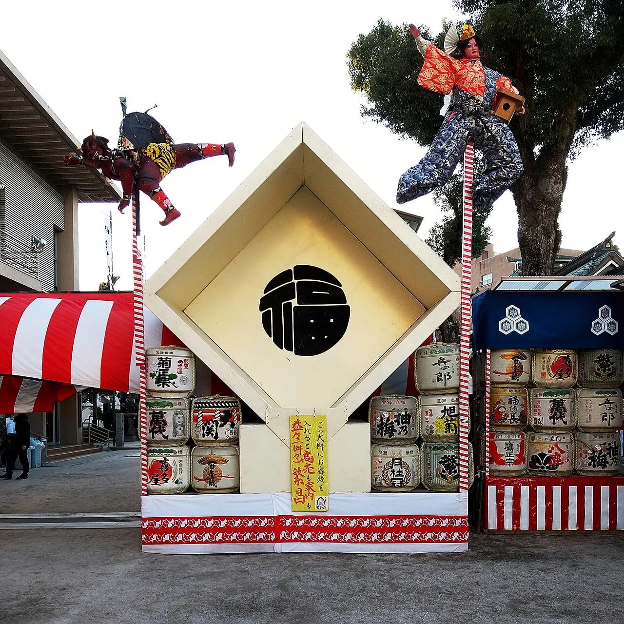 A giant diamond-shaped gate marked with the character for good luck, with demon figures leaping on poles beside it.
