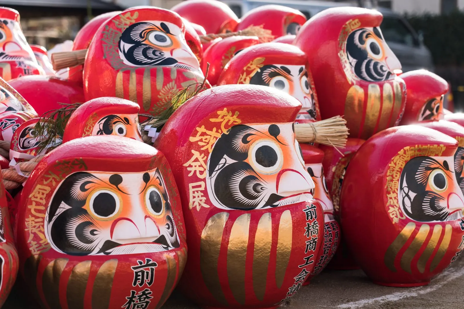 A close view of many bright red daruma dolls with painted gold patterns.