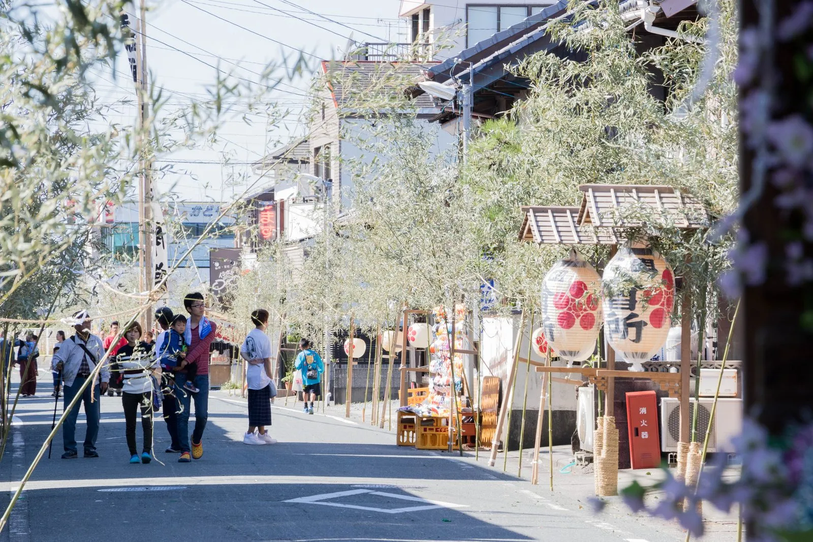 A street in Maisaka decorated with bamboo and lanterns, with a festival float and visitors.