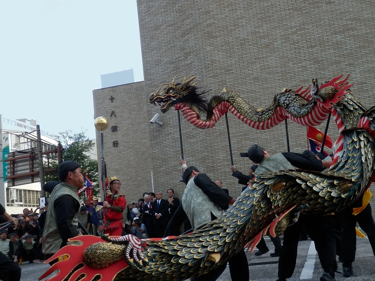Performers on poles move a long green and gold dragon through a square in Nagasaki.