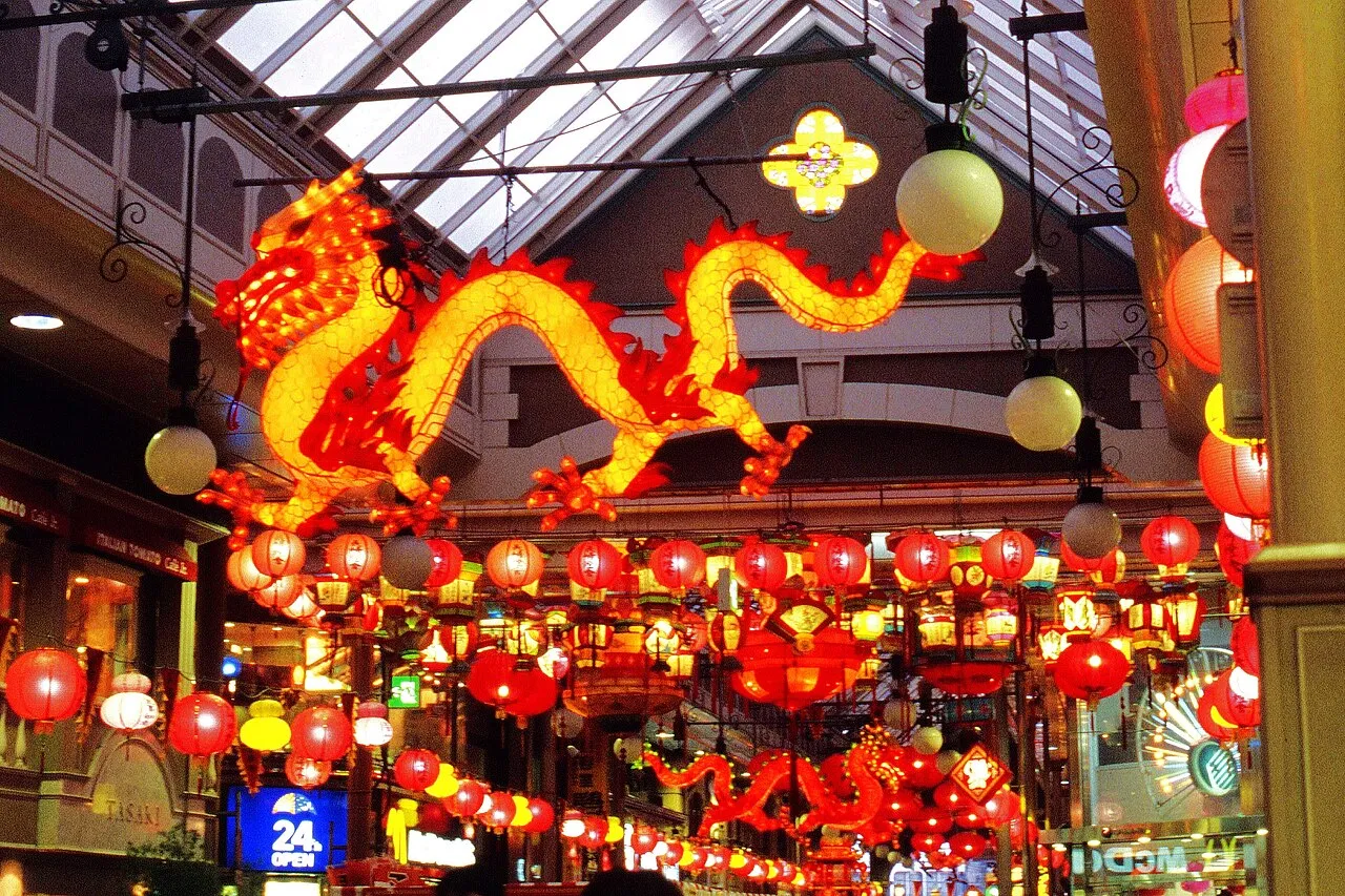 A long golden dragon lantern and rows of red and yellow lanterns hang under the roof of a shopping arcade.