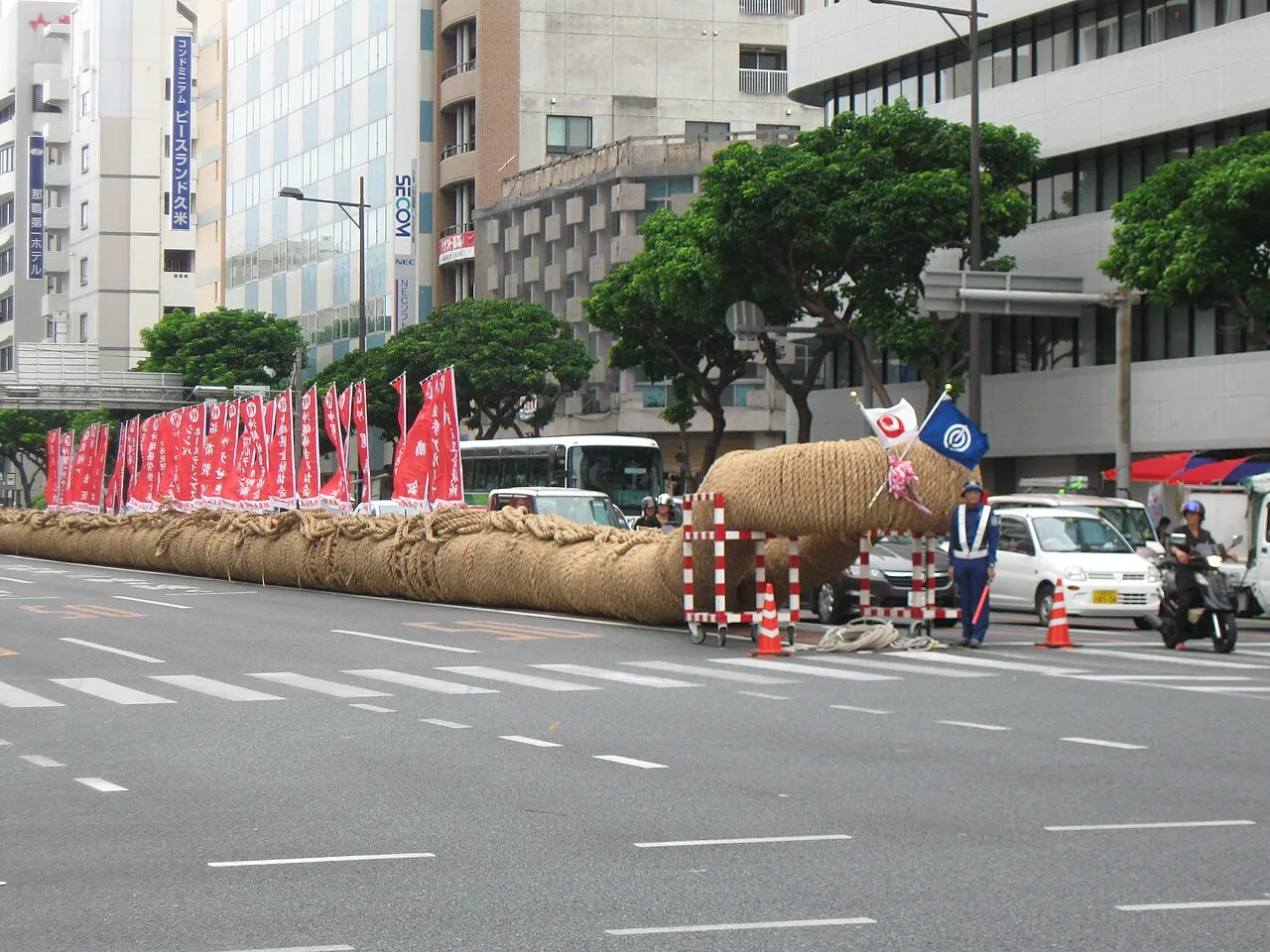 A huge rope of rice straw, as thick as a person is tall, laid along a city avenue lined with red banners.