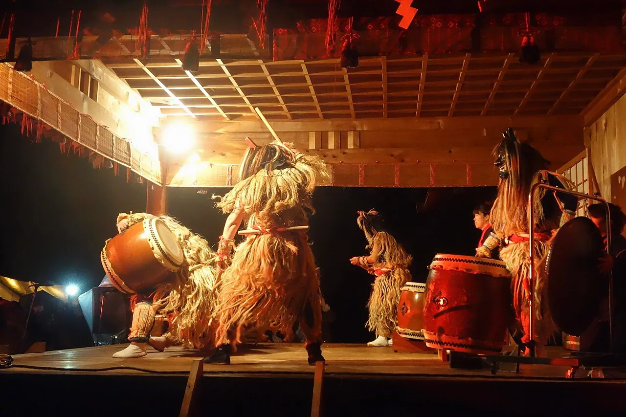 Namahage in shaggy straw costumes and horned masks beat large drums on a lit stage.