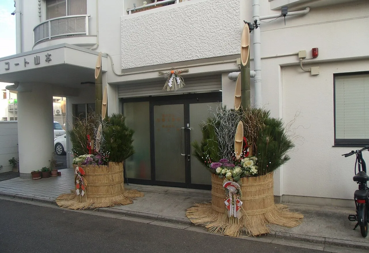 A pair of New Year decorations of cut bamboo, pine and ornamental cabbage in straw-wrapped bases, either side of a doorway with a sacred straw rope above.