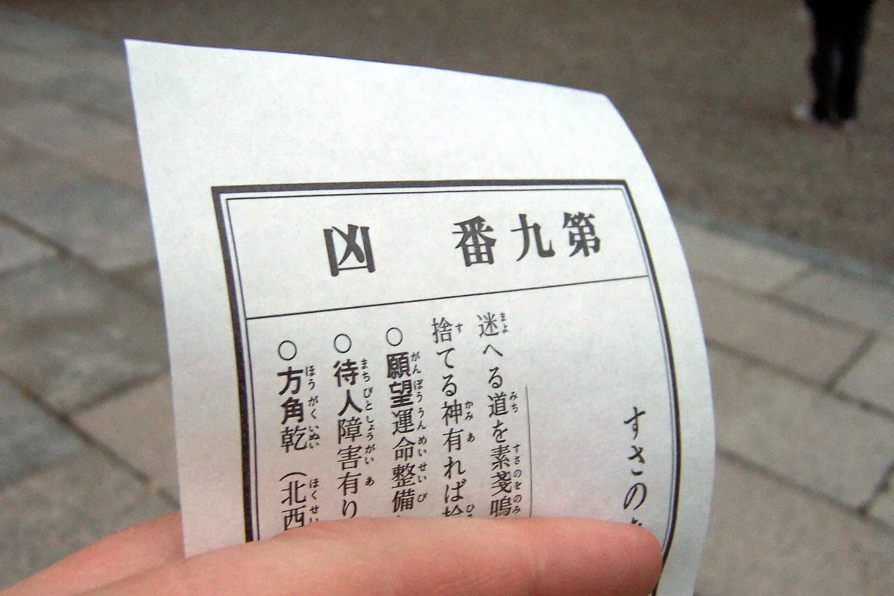 A hand holds a printed paper fortune headed with the character for bad luck.