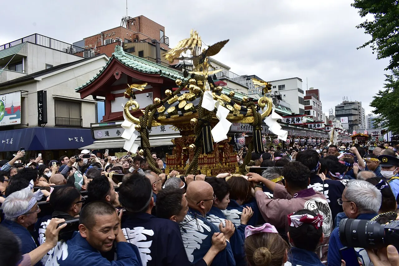 A golden mikoshi topped with a phoenix carried through a packed street in Asakusa.
