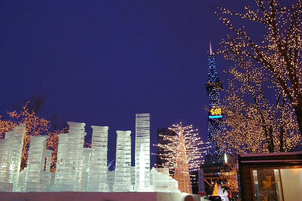 Ice sculptures lit blue at night in Ōdōri Park, with illuminated trees and the Sapporo TV Tower behind.