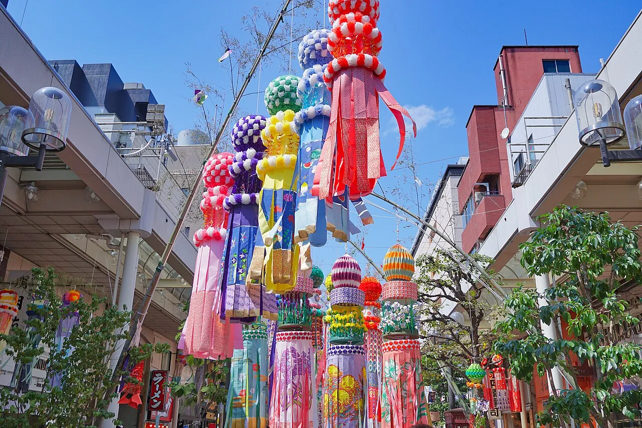 Huge colorful paper streamers hang from bamboo poles in a covered shopping arcade.