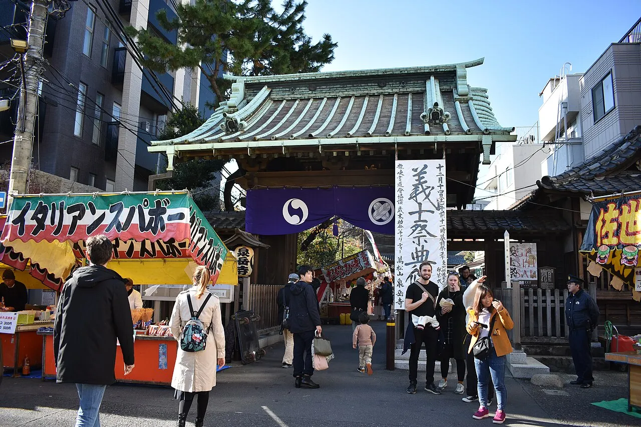 Visitors pass through the tiled gate of Sengaku-ji temple, hung with a purple curtain, with food stalls in front.