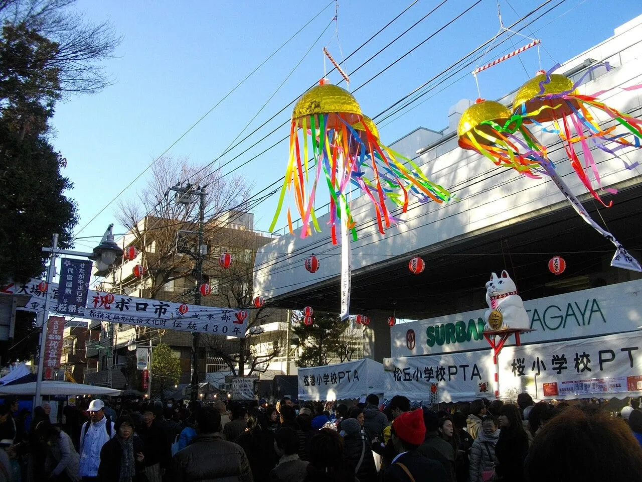 Crowds in a street under festival banners and colourful decorations hanging from a station.