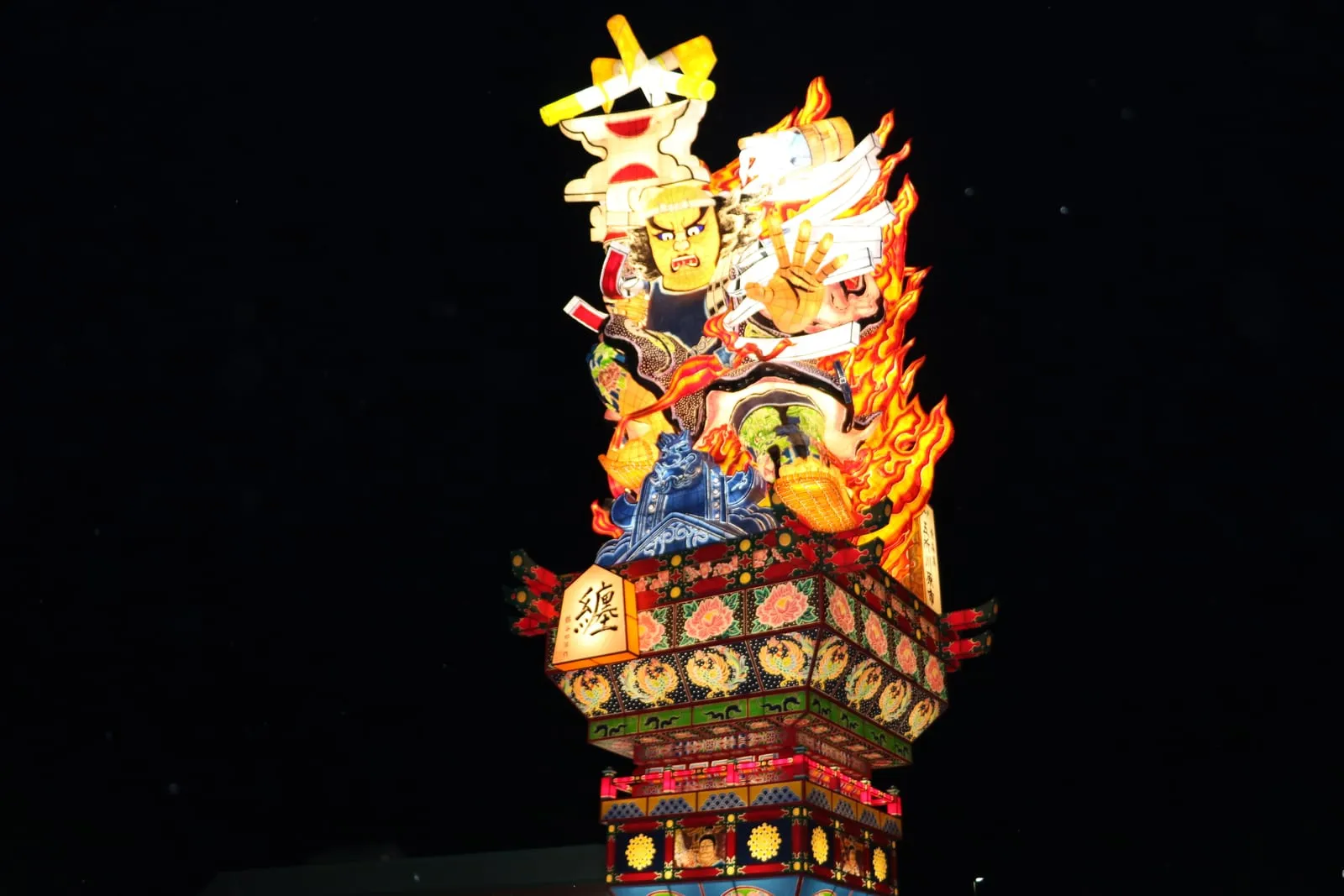 A glowing lantern float of a warrior and flames rises into the black night sky.