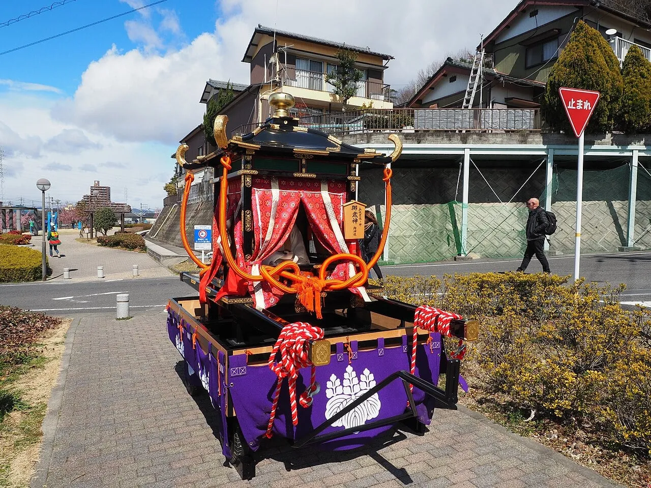 A richly decorated palanquin with red curtains, gold fittings and purple cloth on a wheeled cart.