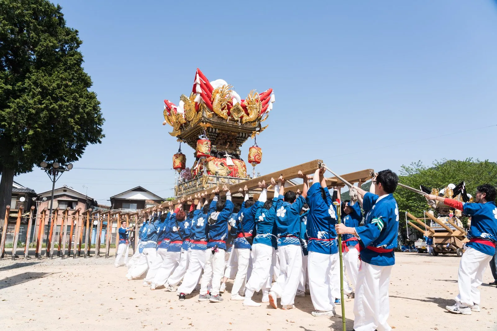 A red and gold drum float carried on long poles by a team in blue and white across the shrine grounds.