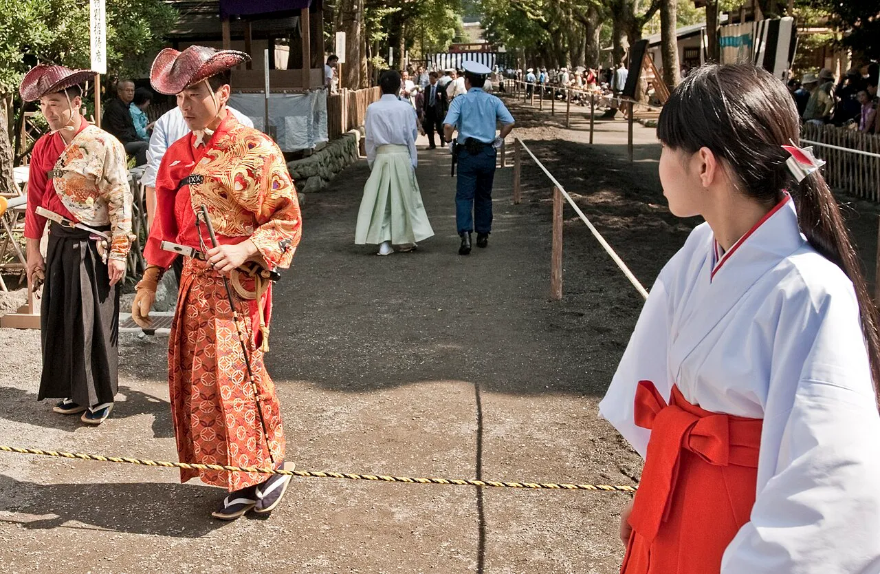 Archers in red hunting robes and wide hats walk along the yabusame track lined with spectators.