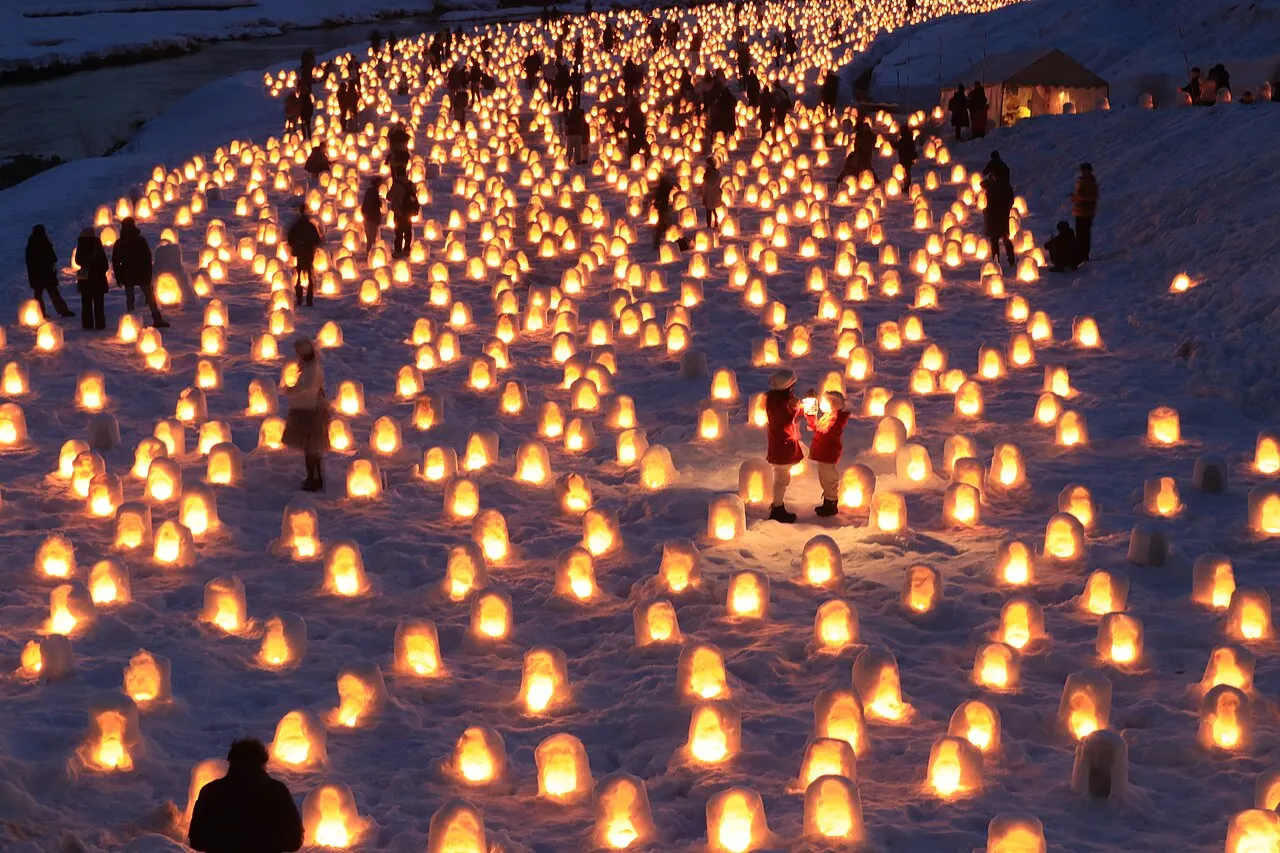Thousands of tiny candlelit snow huts covering a snowy riverbank at dusk.