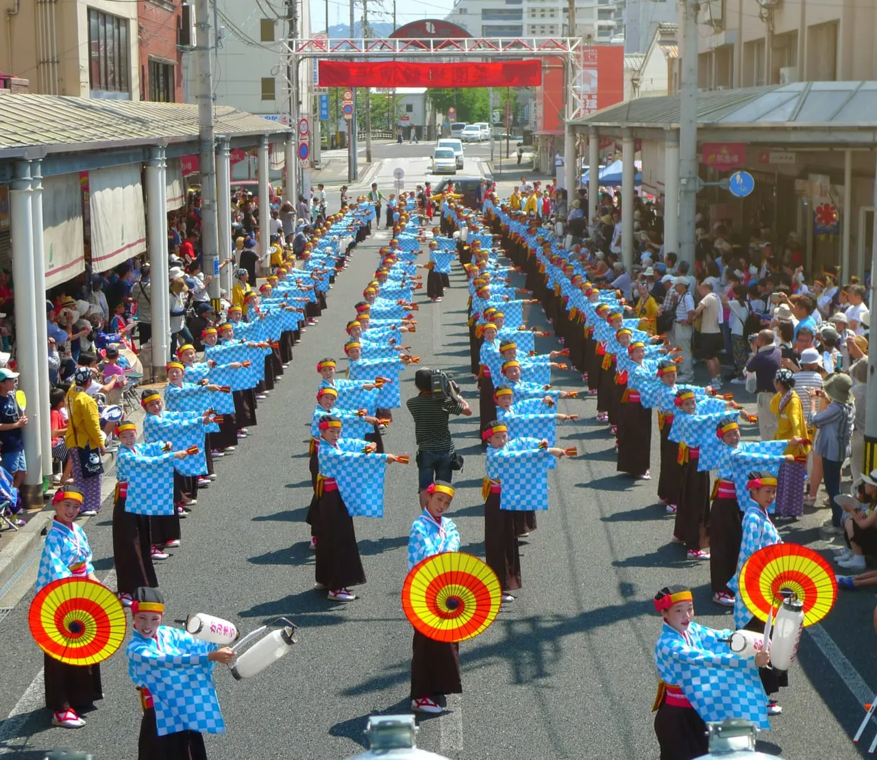 Two long lines of dancers in blue start down a city street lined with spectators.